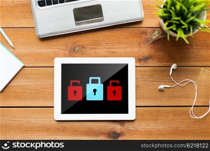 business, cyber protection, web security and technology concept - close up of tablet pc computer, laptop and earphones on wooden table with padlock icons on screen