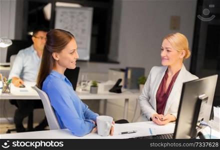 business, deadline and communication concept - businesswomen talking and drinking coffee late at night office. businesswomen drinking coffee at night office