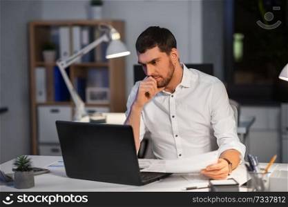 business, deadline and people concept - businessman with laptop computer and papers working at night office. businessman with laptop working at night office