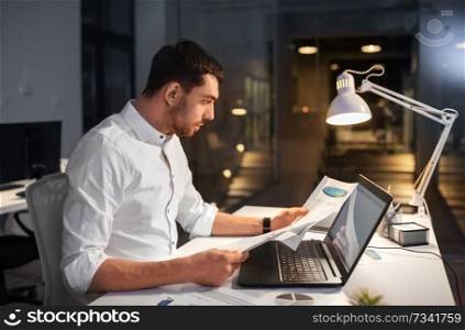 business, deadline and people concept - businessman with laptop computer and papers working at night office. businessman with laptop working at night office