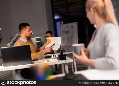 business, deadline and people concept - man showing papers to colleague late at night office. business team with papers working late at office