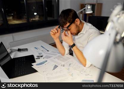business, deadline and stress concept - tired businessman in glasses working at night office. tired businessman working at night office