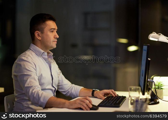 business, deadline and technology concept - businessman with computer working at night office. businessman with computer working at night office