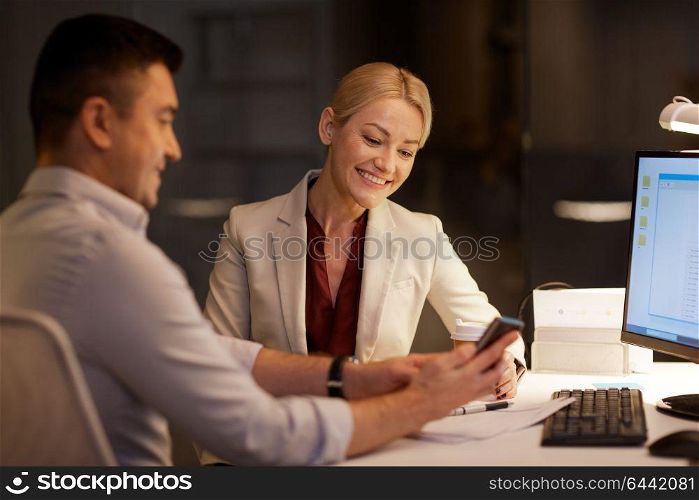 business, deadline and technology concept - businesswoman and businessman or coworkers with smartphone having coffee break late at night office. business people with smartphone at night office