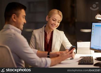 business, deadline and technology concept - businesswoman and businessman or coworkers with smartphone having coffee break late at night office. business people with smartphone at night office