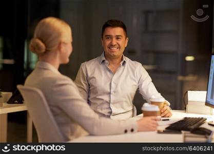 business, deadline and technology concept - businesswoman and businessman talking and drinking coffee late at night office. business people drinking coffee at night office