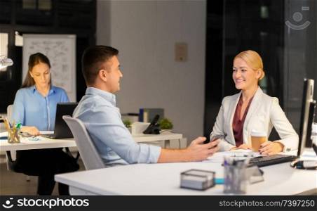 business, deadline and technology concept - businesswoman and businessman talking and drinking coffee late at night office. business people drinking coffee at night office