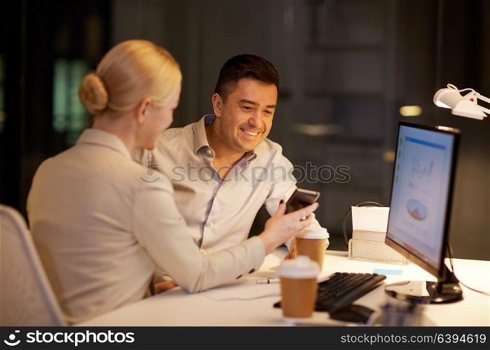 business, deadline and technology concept - businesswoman and businessman with smartphone having coffee break late at night office. business people with smartphone at night office