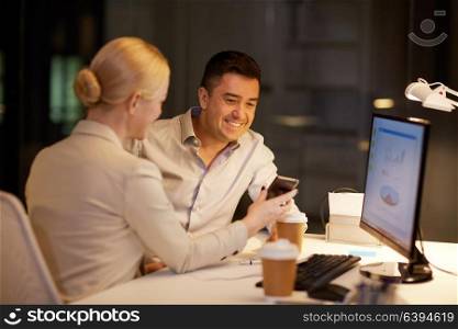 business, deadline and technology concept - businesswoman and businessman with smartphone having coffee break late at night office. business people with smartphone at night office