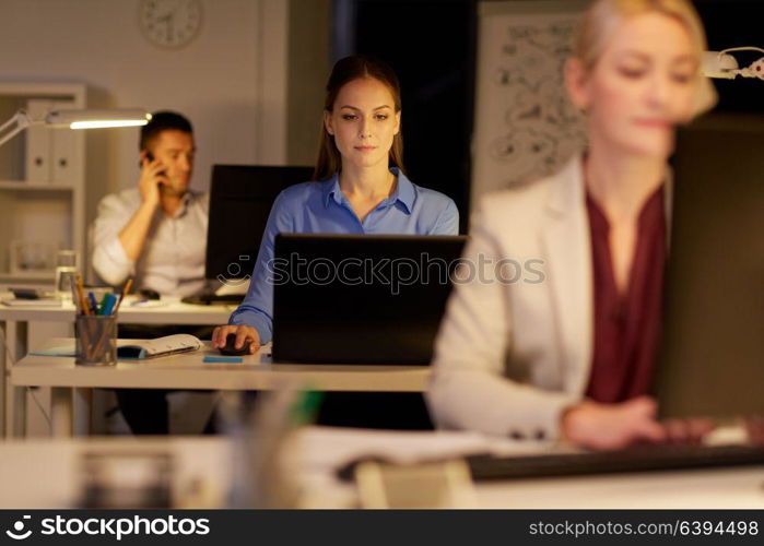 business, deadline and technology concept - businesswoman with laptop computer working at night office. businesswoman at computer working at night office
