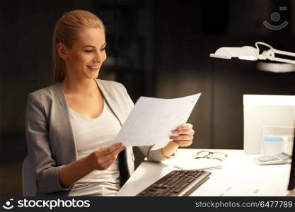 business, deadline and technology concept - businesswoman with papers and computer working at night office. businesswoman with papers working at night office. businesswoman with papers working at night office
