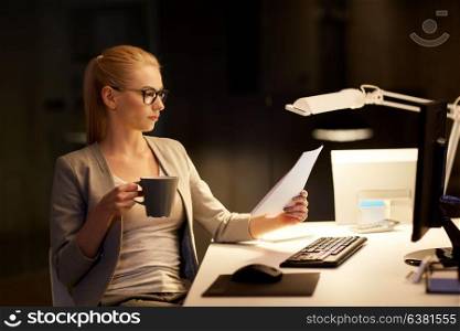 business, deadline and technology concept - businesswoman with papers computer working at night office and drinking coffee. businesswoman with papers working at night office
