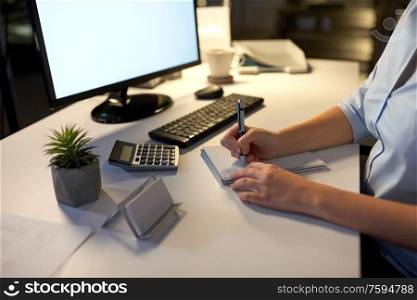business, deadline and technology concept - businesswoman writing to notebook at night office. businesswoman writing to notebook at night office