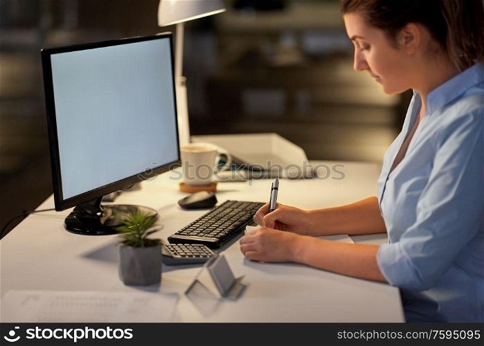 business, deadline and technology concept - businesswoman writing to notebook at night office. businesswoman writing to notebook at night office