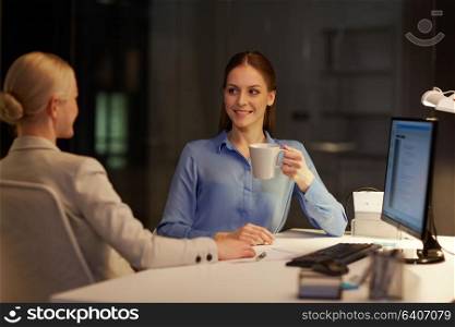 business, deadline and technology concept - businesswomen talking and drinking coffee late at night office. businesswomen drinking coffee at night office
