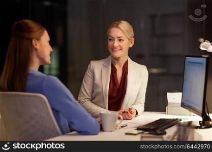 business, deadline and technology concept - happy businesswomen or coworkers talking late at night office. happy businesswomen talking late at night office