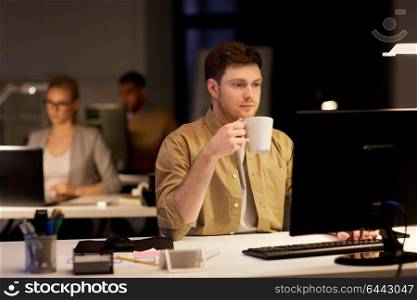 business, deadline and technology concept - man with computer working and drinking coffee at night office. man with laptop and coffee working at night office