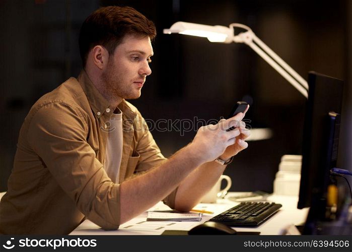 business, deadline and technology concept - man with smartphone and computer working at night office. man with smartphone working late at night office