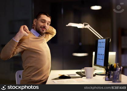 business, deadline and technology concept - tired man with computer working and stretching at night office. man with computer working late at night office