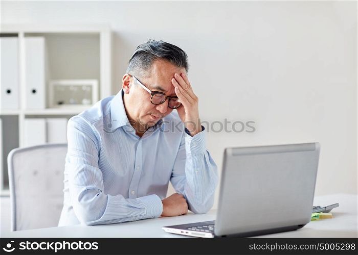 business, deadline, stress, people and technology concept - businessman in eyeglasses with laptop computer suffering from headache at office. businessman in eyeglasses with laptop at office