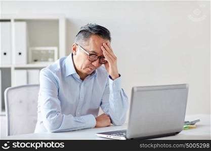 business, deadline, stress, people and technology concept - businessman in eyeglasses with laptop computer suffering from headache at office. businessman in eyeglasses with laptop at office