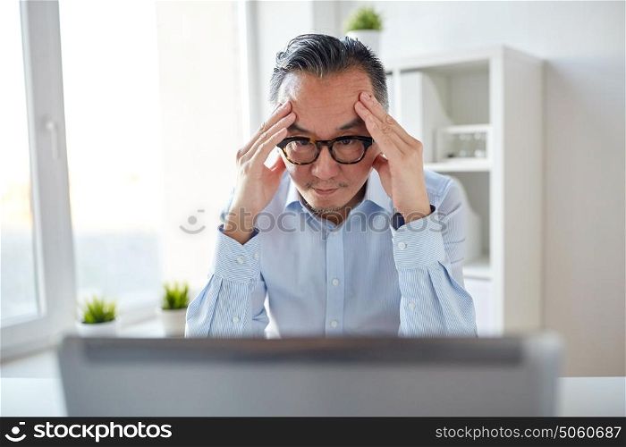 business, deadline, stress, people and technology concept - businessman in eyeglasses with laptop computer at office. businessman in eyeglasses with laptop at office
