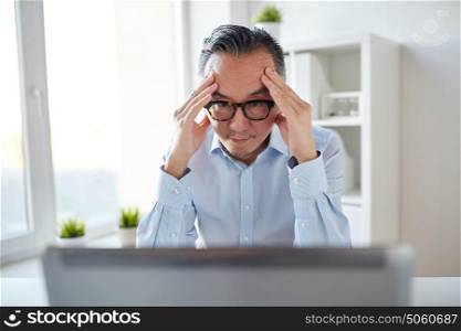 business, deadline, stress, people and technology concept - businessman in eyeglasses with laptop computer at office. businessman in eyeglasses with laptop at office