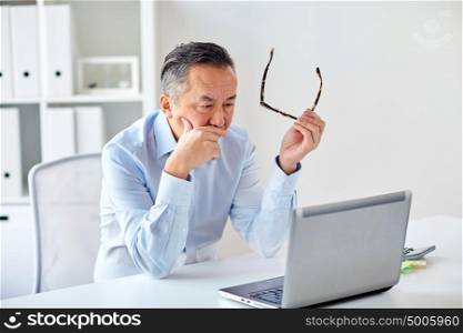 business, deadline, stress, people and technology concept - businessman with eyeglasses and laptop computer at office. businessman with eyeglasses and laptop at office
