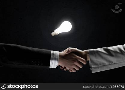 Business deal. Business partners handshake and glowing light bulb