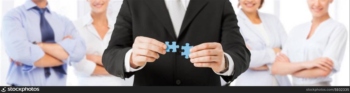 business, development, team building and people concept - close up of man trying to connect puzzle pieces over group of partners background