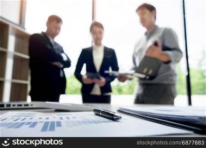 business document in touchpad lying on the desk, office workers discussting meeting in the background
