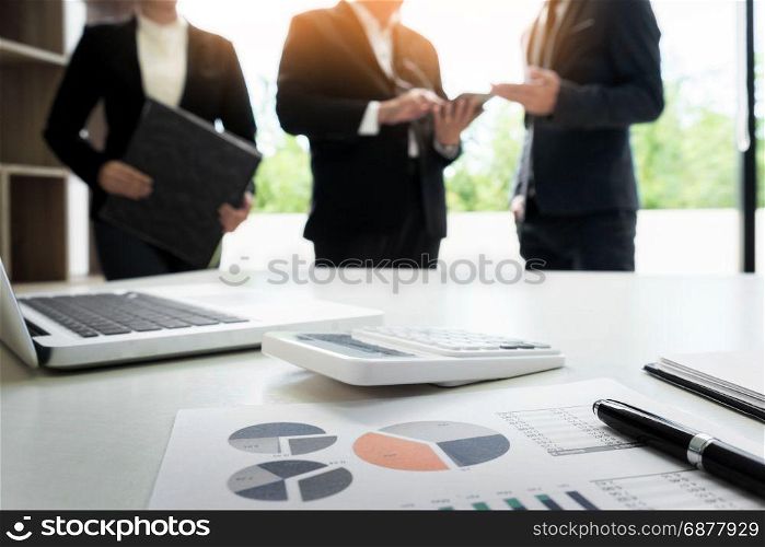 business document in touchpad lying on the desk, office workers discussting meeting in the background