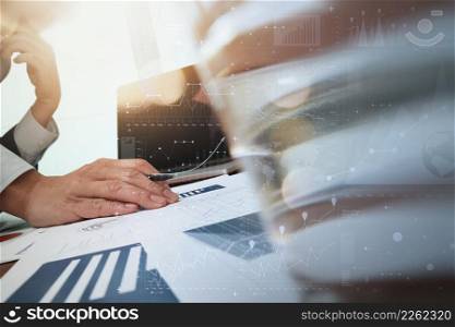 business documents on office table and laptop computer and graph business with digital layer effect and man working in the background and glass of water foreground