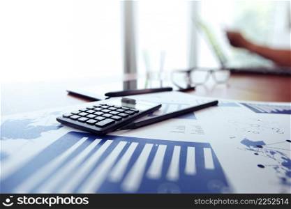 business documents on office table with calculator and digital tablet and man working in the background
