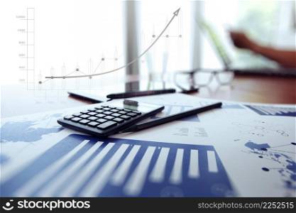 business documents on office table with digital tablet and man working with smart phone in the background with business graph diagram concept