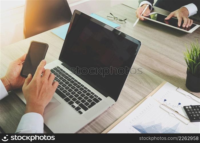 business documents on office table with smart phone and blank screen laptop computer and graph business diagram and two colleagues discussing data in the background