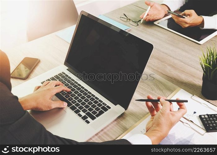 business documents on office table with smart phone and blank screen laptop computer and graph business diagram and two colleagues discussing data in the background