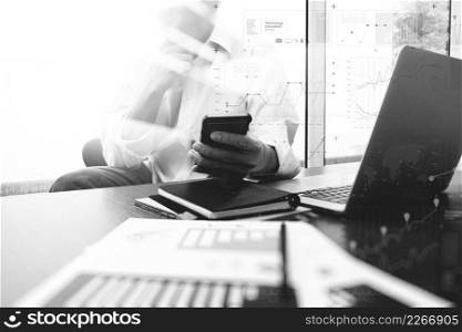 business documents on office table with smart phone and digital laptop computer and graph business diagram and man working in the background,black and white  