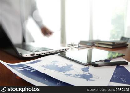 business documents on office table with smart phone and digital tablet and man working in the background