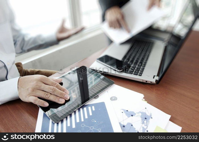 business documents on office table with smart phone and digital tablet and stylus and two colleagues discussing data in the background