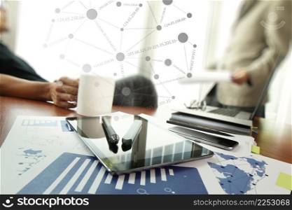 business documents on office table with smart phone and digital tablet and stylus and two colleagues discussing data in the background