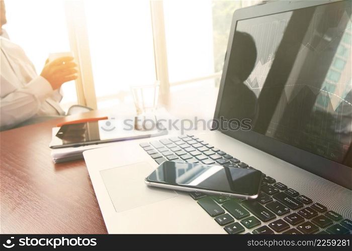 business documents on office table with smart phone and digital tablet and graph business diagram and man holding a cup of coffee in the background