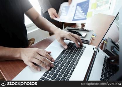 business documents on office table with smart phone and digital tablet and laptop computer and two colleagues discussing data in the background