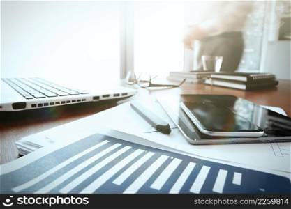 business documents on office table with smart phone and digital tablet and graph business diagram and man working in the background and social media diagram