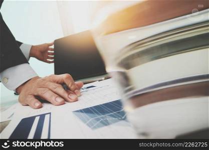 business documents on office table with smart phone and laptop computer and graph business with digital layer effect and man working in the background