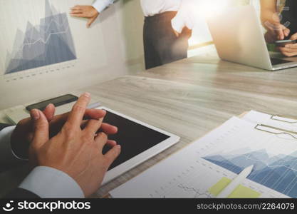 business documents on office table with smart phone and laptop computer and graph business with social network diagram and three colleagues discussing data in the background