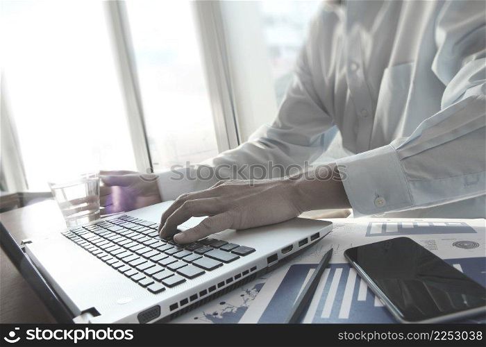 business documents with smart phone on office table and business man hand working on laptop computer on wooden desk as concept
