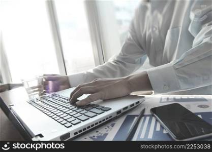 business documents with smart phone on office table and business man hand working on laptop computer on wooden desk as concept