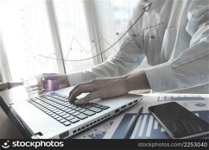 business documents with smart phone on office table and business man hand working on laptop computer on wooden desk as concept and graph business diagram
