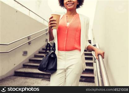 business, drinks, lifestyle and people concept - close up of young smiling african american businesswoman with coffee cup walking downstairs to city subway